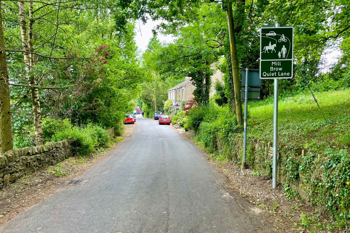 "Quiet Lane" sign on a rural lane at Mill Brow near Marple Bridge. The sign shows a car, cyclist, horse and pedestrians, denoting a hierarchy of patience amongst users.
