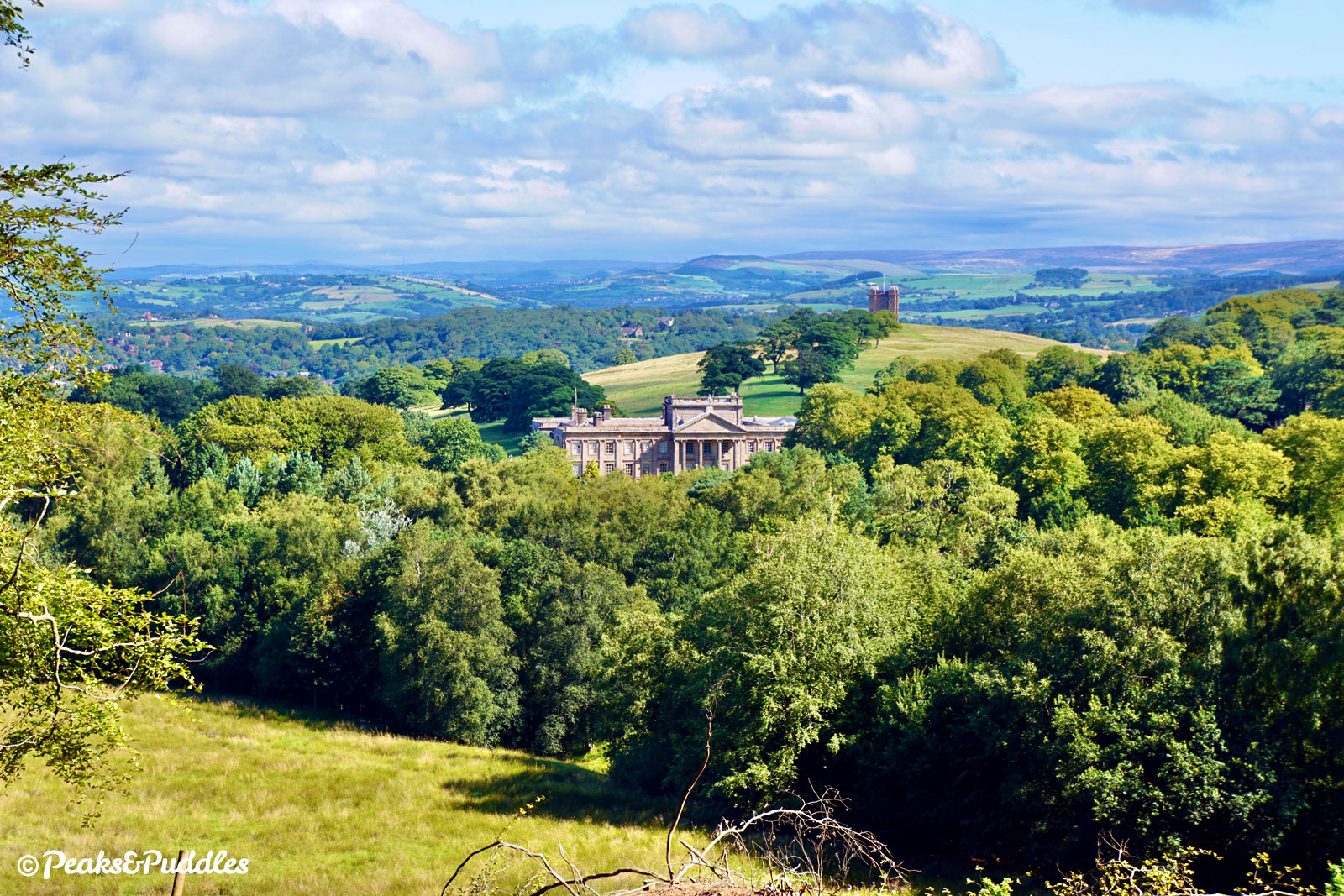 In this famous view of both Lyme Hall and The Cage, seen from the footpath through Knightslow Wood, Marple Ridge is the hill extending directly behind, to the left.